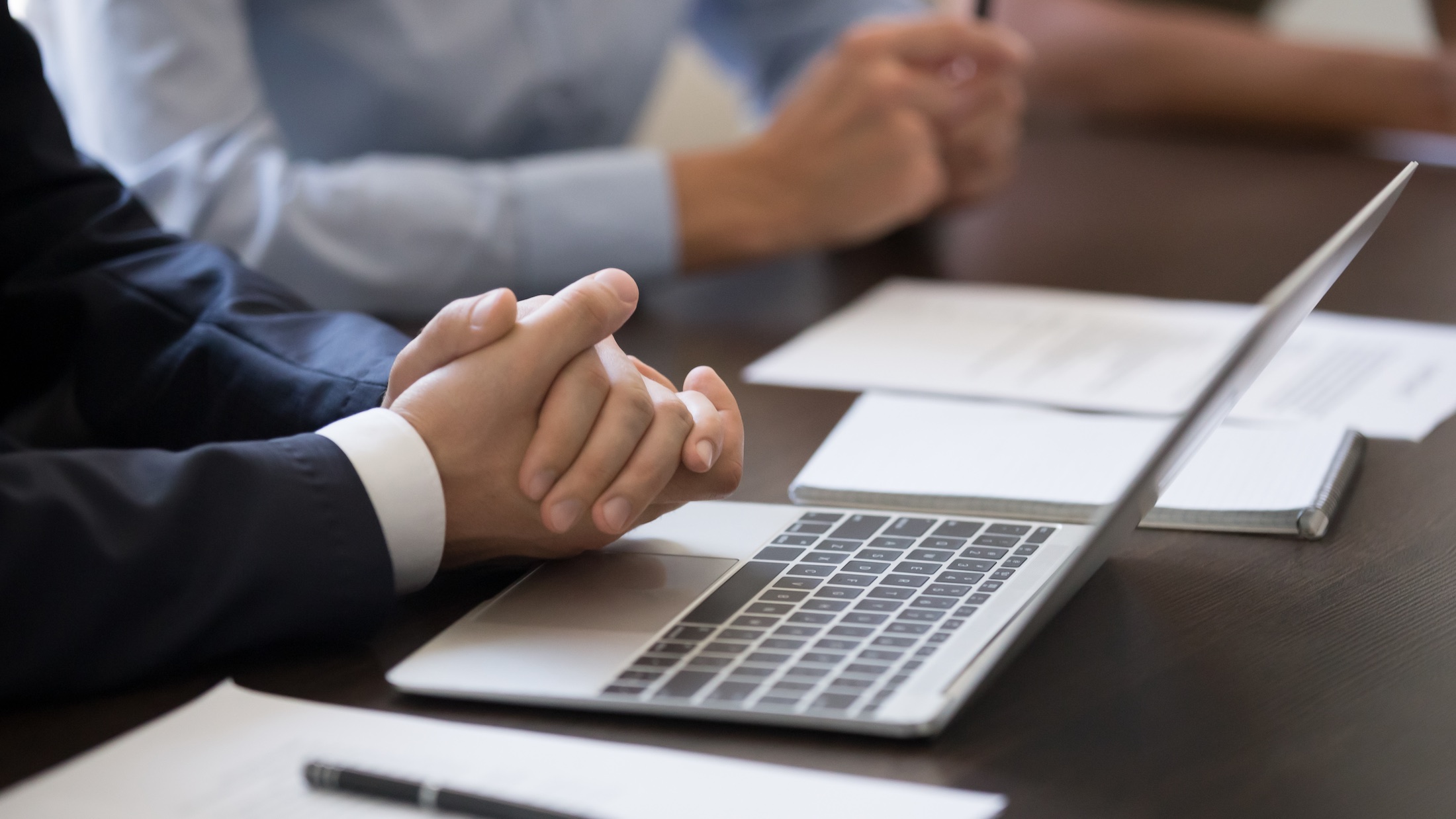 Businesspeople gather at formal meeting, investors partners sitting in boardroom desk focused on listening speaker presenting startup new project cropped image hands documents and laptop close up view