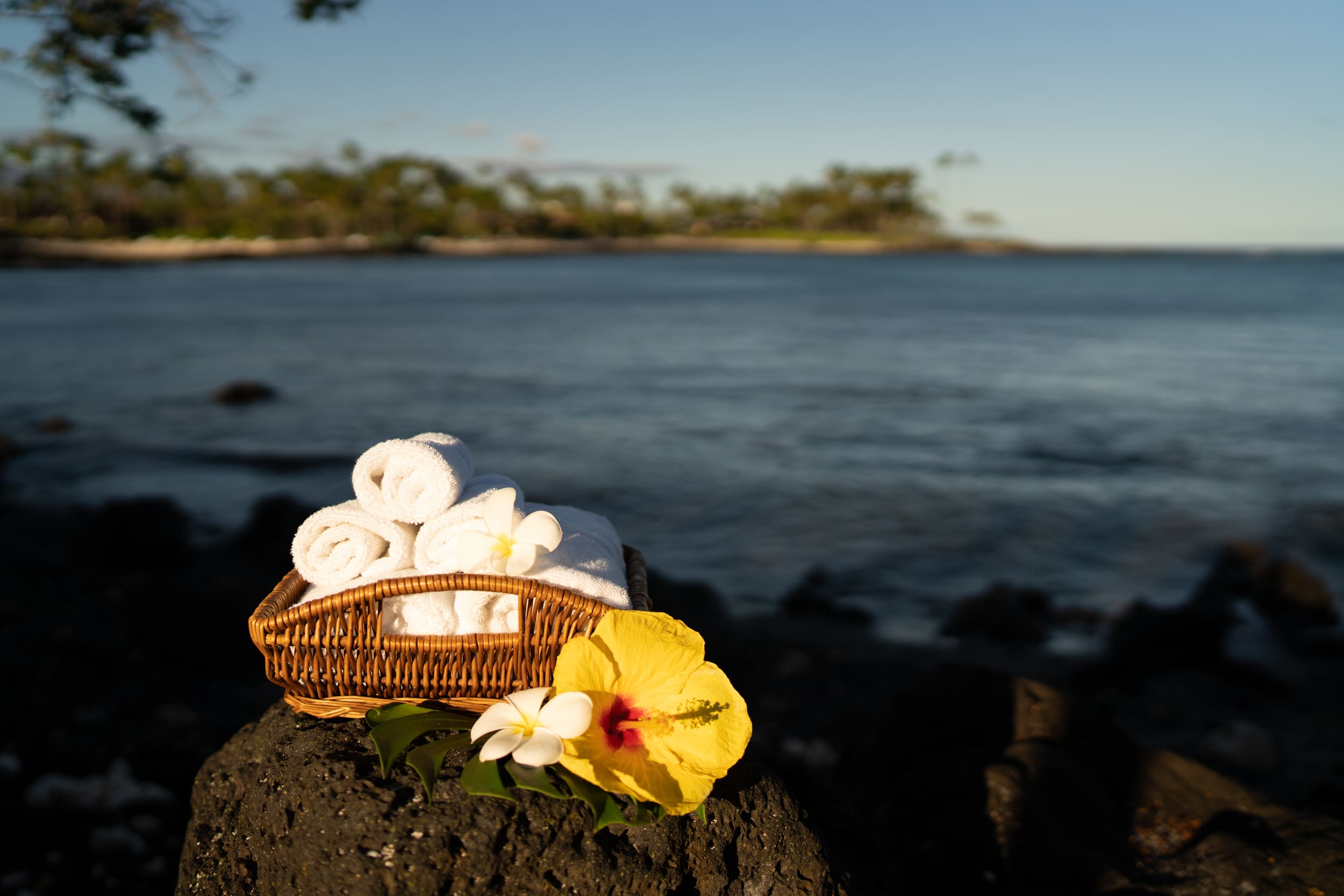 basket of towels sitting on a rock next to the ocean