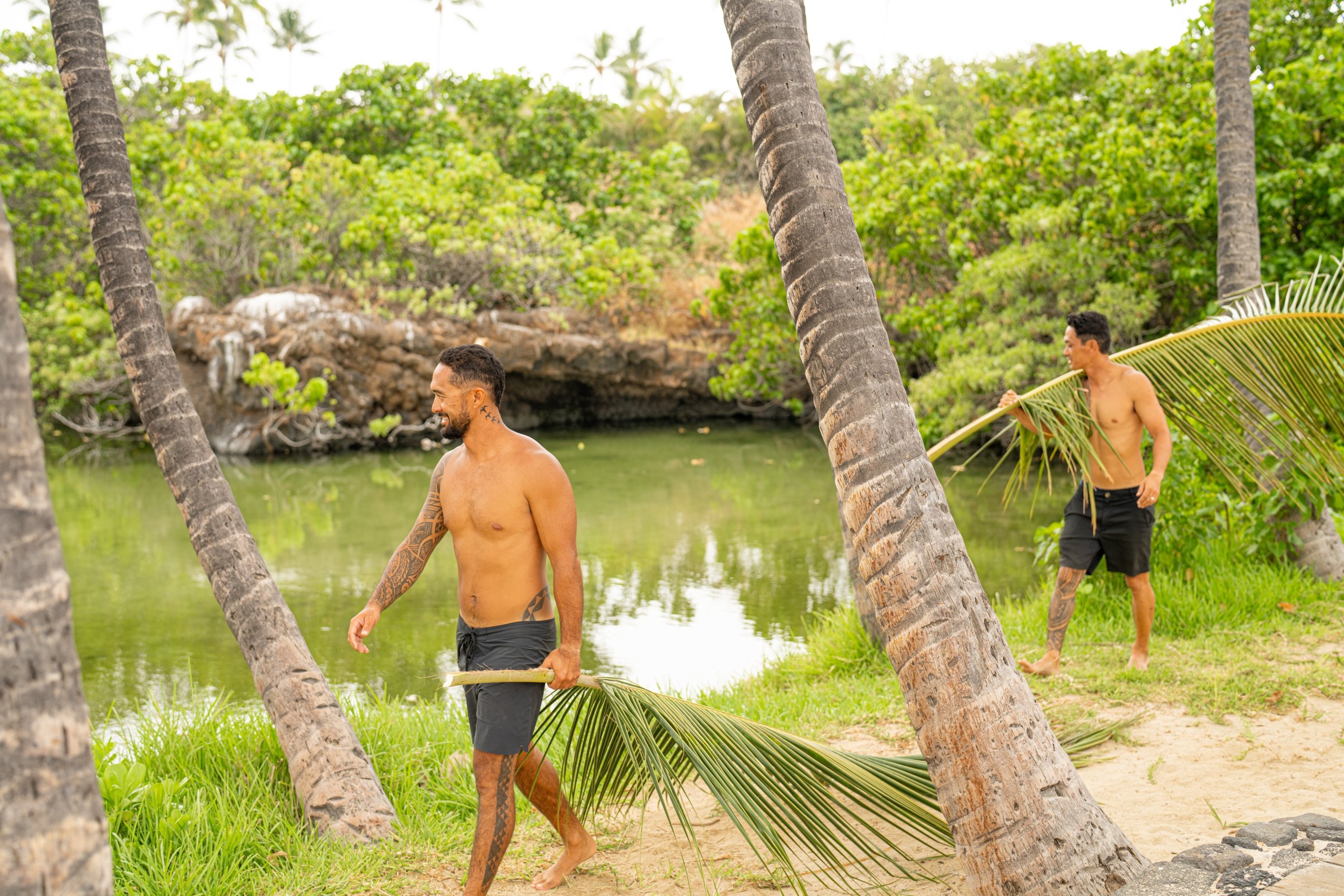 Two men walking by pond with palm fronds at Fairmont Orchid, Hawaii