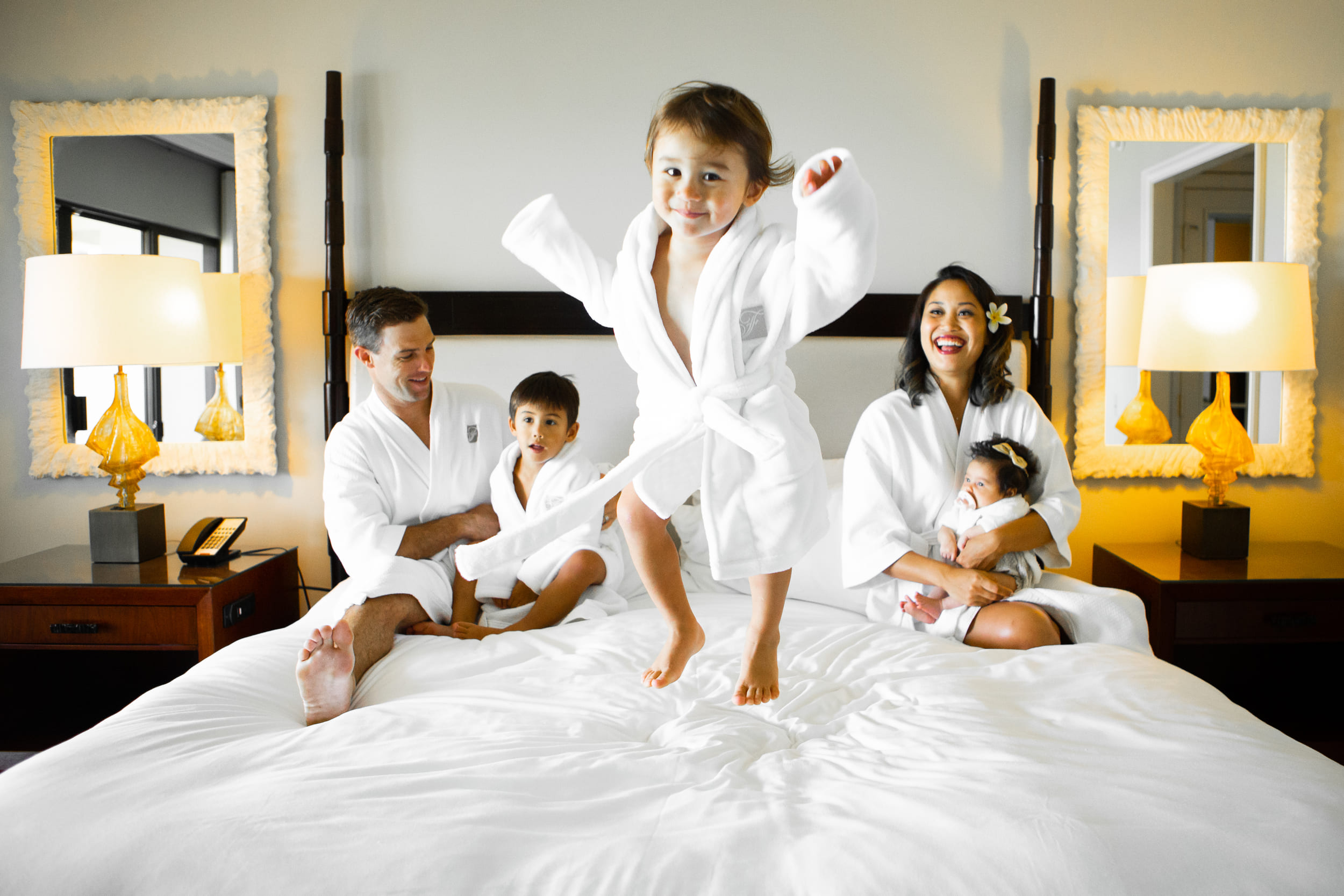 little boy jumping on a bed with his family in the background