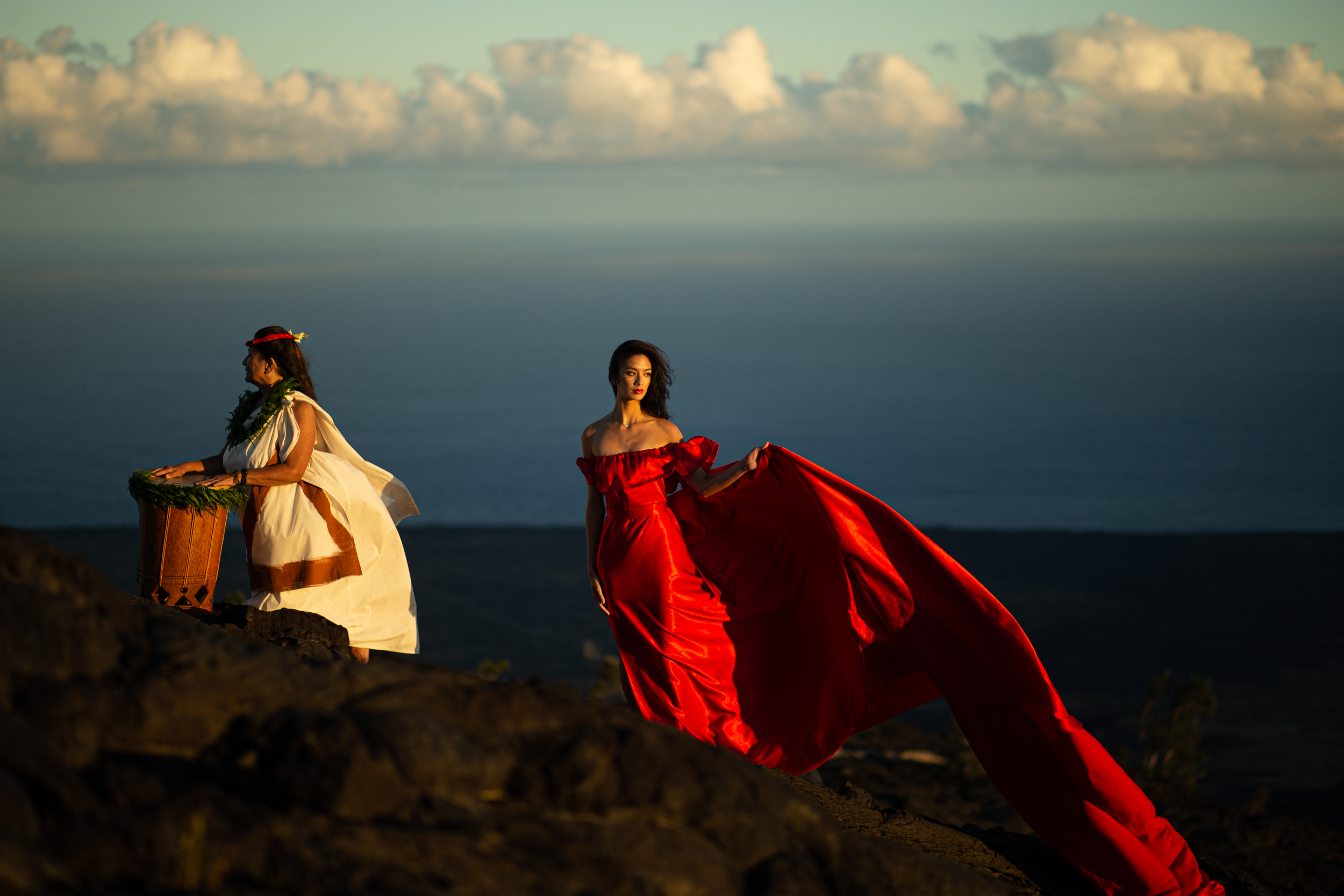 Woman in red dress and woman playing drum on cliff side