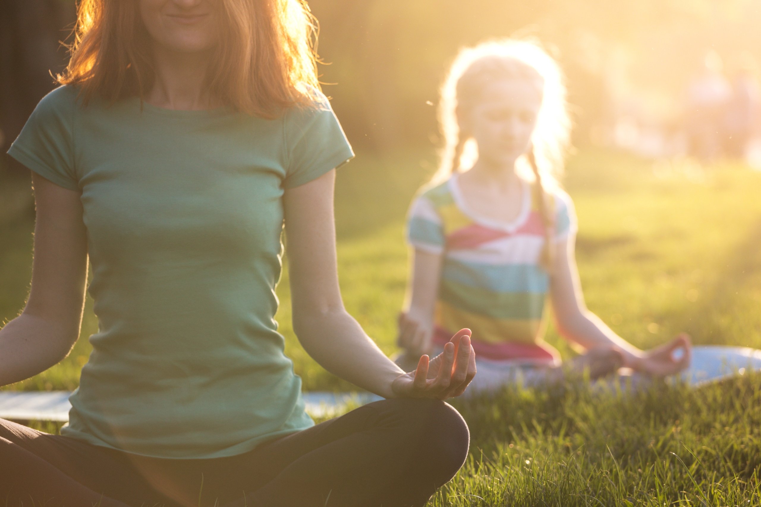 Woman and young girl practicing yoga pose, sitting in the grass